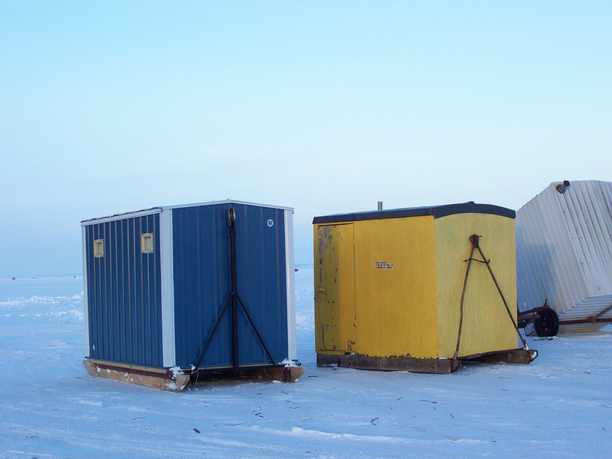 Two ice shanties, one blue and one yellow, standing on the frozen surface of Lake Winnebago with more visible in the distance